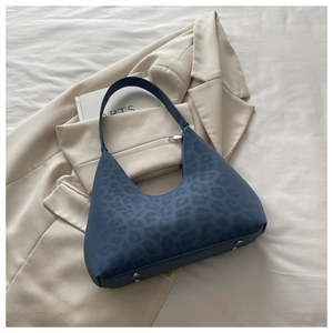 Top view of a navy leopard print crescent shoulder bag on a beige textured background