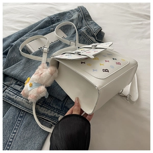 Détail d'un sac bandoulière blanc en PU avec imprimé B et breloque en peluche