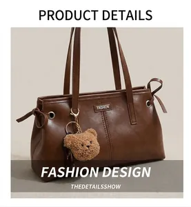 Detailed close-up of dark brown leather tote bag with metal label and plush bear charm