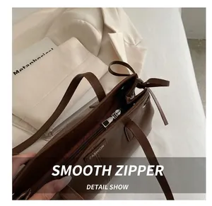 Detailed view of brown leather tote bag showing smooth metal zipper and fashion label