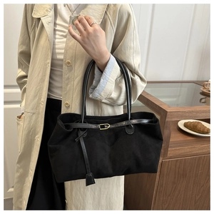 Détail d'un grand sac cabas en daim noir avec poignées en cuir et pampille décorative