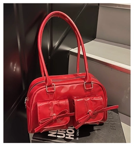 Detail of red patent leather shoulder bag with bow-decorated pockets on black display