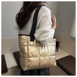 Detailed side view of champagne gold quilted tote bag with black strap on model