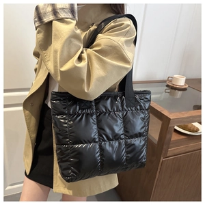 Detail of black quilted tote bag with glossy finish shown on model in cafe setting