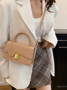 Elegante borsa a tracolla in pelle beige con chiusura dorata e ciondolo su blazer bianco