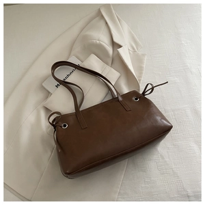 Detailed close-up of brown faux leather tote bag with side bow ties on white jacket