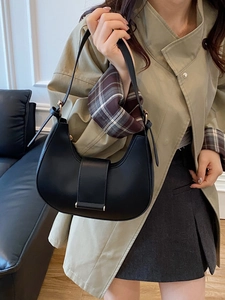 Minimalist black crescent shoulder bag with leather strap and gold buckle on a chic model