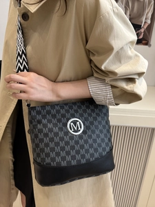 Sac seau noir chic avec imprimé M gris et bandoulière tissée porté sur un trench-coat