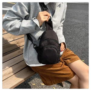Outdoor shot of a black nylon crossbody chest bag with adjustable strap and dual front pockets
