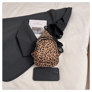 Leopard print canvas waist bag with adjustable strap shown alongside a notebook and suit