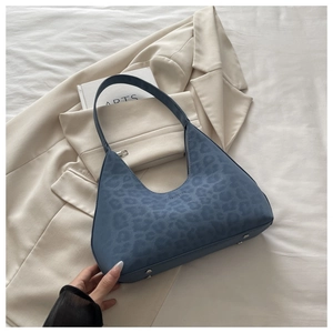 Blaue Hobo-Tasche mit Leopardenmuster und Metallfüßen auf beigefarbenem Stoff