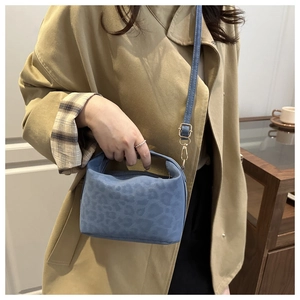 Detail view of blue leopard print mini bag with golden metal hardware on brown coat