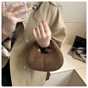 Detail of a dark brown suede crescent handbag showing texture and gold zipper closure