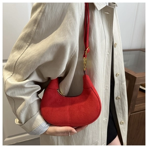 Detail of red suede half-moon hobo bag with gold hardware worn with a beige coat