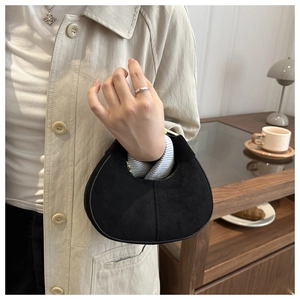Detail of a vintage black suede half-moon bag held by a model in a cozy cafe setting