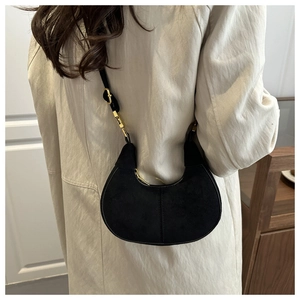 Detail of a black suede crescent hobo bag with gold zipper on a beige coat
