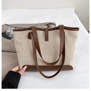 Detail of canvas tote bag showing beige fabric and brown leather handle contrast