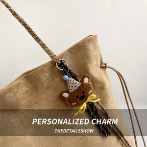 Detail of brown suede bucket bag with gold chain strap and cute bear charm accessory