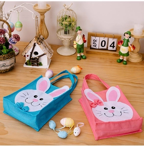 Pink and blue Easter bunny gift bags with white rabbit appliques on wooden table