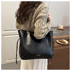 Chic black leather chain bucket bag styled with a beige sweater and white skirt