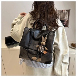 Detailed back view of a black leather backpack with a decorative plush rabbit charm