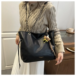 Détail du sac cabas noir avec bandoulière chaîne, breloque ours et logo en cuir élégant