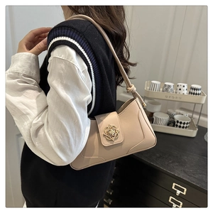 Detail of beige crescent shoulder bag featuring a gold flower clasp worn by a model