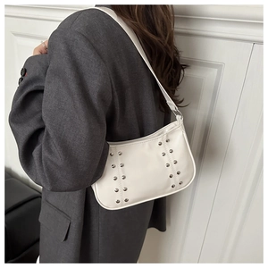 Détail du sac bandoulière en cuir blanc avec clous argentés sur un blazer foncé