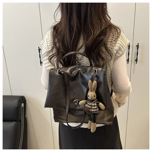 Detail of dark brown leather backpack with turn-lock closure and knitted rabbit charm