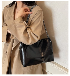 Detail of black patent leather flap bag with metallic chain strap and embossed logo