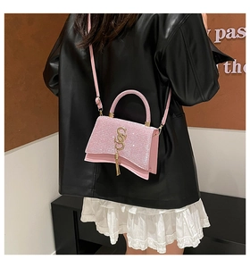 Detail of pink glitter crossbody bag with gold logo and long fringe tassel on black leather