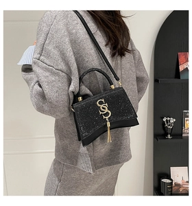Detail of black sequined handbag with gold SS logo and fringe worn by a model