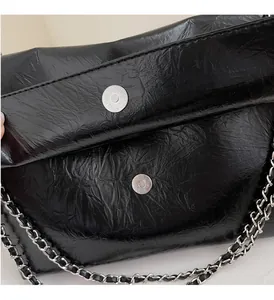 Detail view of glossy black crinkled texture tote with silver chain strap and magnetic closure