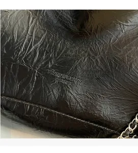 Detail of black wrinkled leather bag featuring embossed text and silver chain strap
