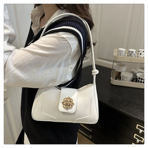 Detail of white leather baguette bag featuring a gold floral buckle and knotted shoulder strap