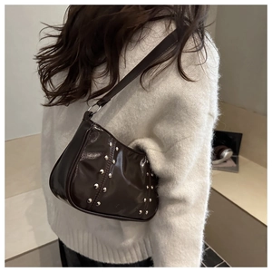Détail du sac brillant marron foncé avec rivets argentés porté sur un pull blanc
