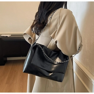 Detail of glossy black pleated PU leather tote bag with thick silver chain strap worn by model