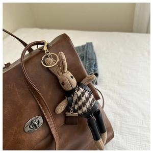 Detail of bunny bag charm in houndstooth vest hanging on a brown leather handbag