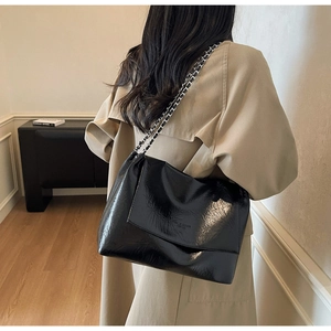 Detail view of the black glossy leather texture and woven chain strap on a tote bag