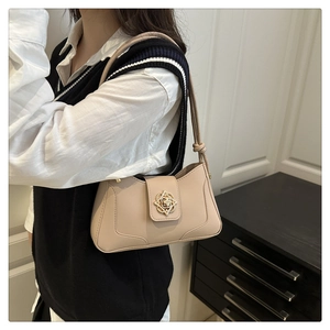 Detail of beige shoulder bag featuring a gold floral clasp and leather strap on a model
