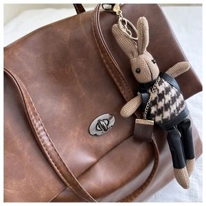 Close-up of handmade knit bunny charm with houndstooth vest on a leather backpack