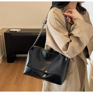 Close-up of black pleated patent leather bag with silver chain strap and flap closure