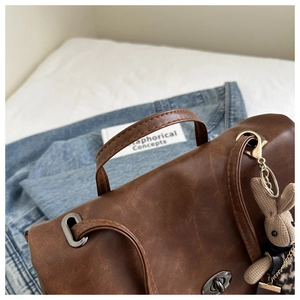 Detail of vintage brown leather backpack featuring a metal twist lock and rabbit charm
