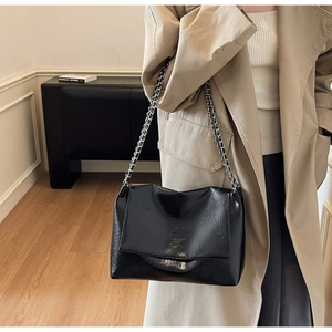 Detail of black wrinkled patent leather shoulder bag with silver chain strap on model