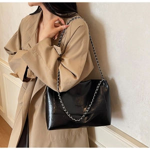 Detail of black glossy wrinkled leather tote with silver chain strap on a model