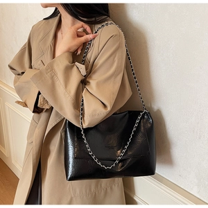 Detail of black crinkled patent leather shoulder bag with silver chain strap and metal finish