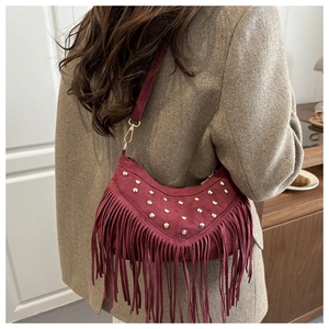 Detail of burgundy suede hobo bag with gold studs and long fringe tassels on surface