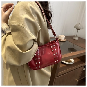 Détail du sac à bandoulière en cuir verni rouge avec rivets argentés et fini brillant