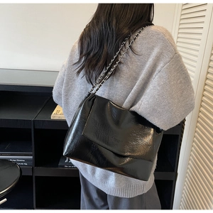 Detail of glossy wrinkled leather texture and silver chain strap on a black shoulder bag