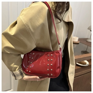 Détail du sac porté épaule en cuir verni rouge avec clous argentés sur trench beige